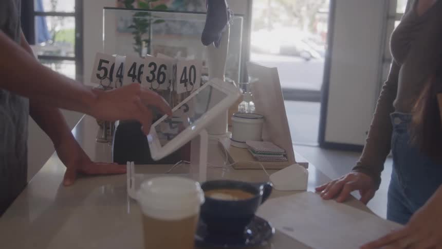 Customer makes a payment at a digital register while two drinks sit on the counter