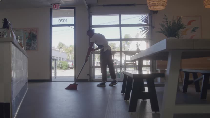 A worker sweeps the floor inside a cafe near the entrance