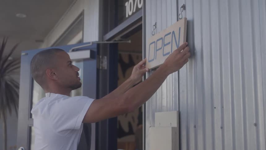 Man hangs an open sign at the entrance of a store