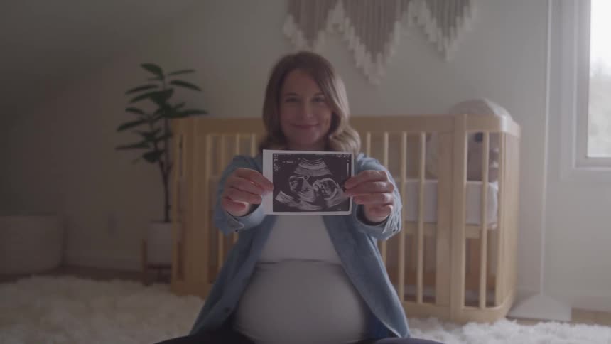 Pregnant woman sitting shows an ultrasound in front of the baby crib