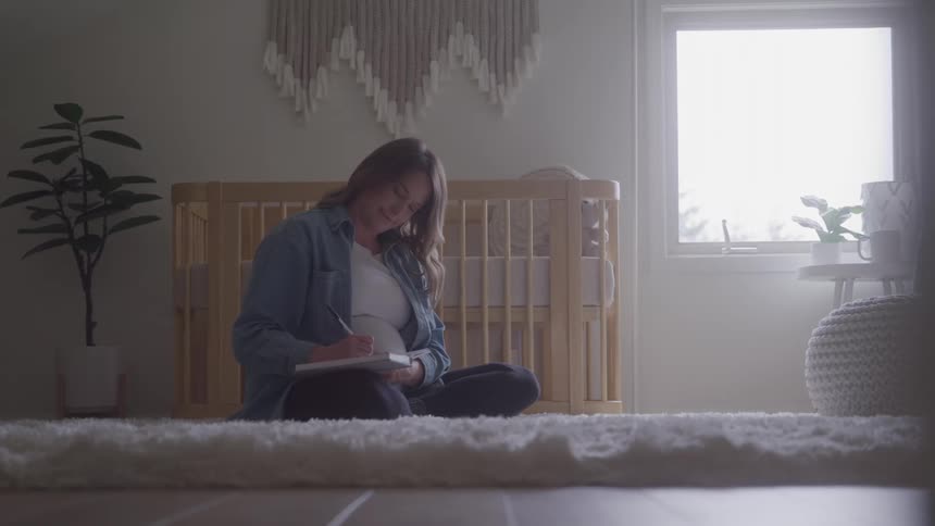 Woman sitting on the floor writes in a notebook beside a crib