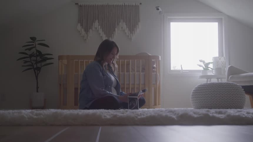 A pregnant woman goes through her pregnancy ultrasound images while sitting on the floor in a room during daytime