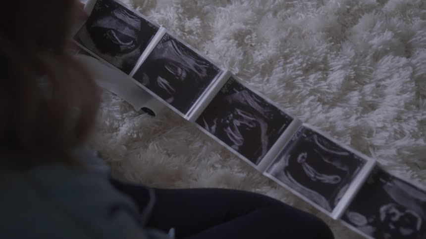 A female seen from behind holds up several ultrasound images while sitting on a fluffy white rug