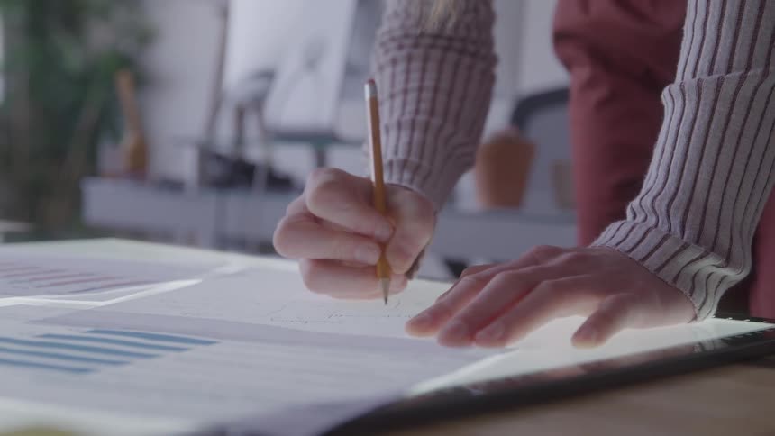 Person writes with a pencil on charts at a work desk