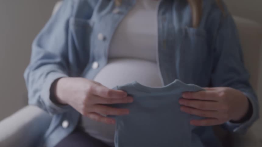 Pregnant body holds a blue baby onesie