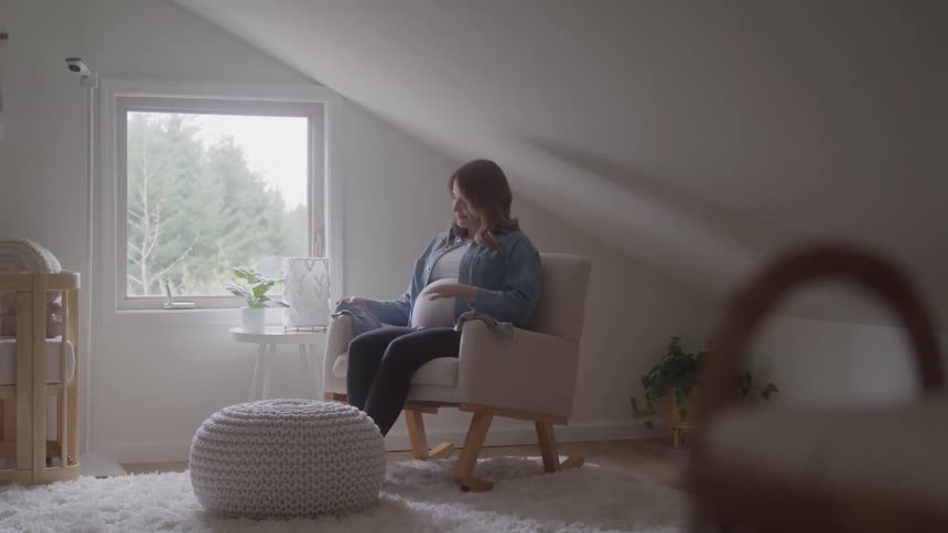 A pregnant woman looks at her new baby clothes indoors