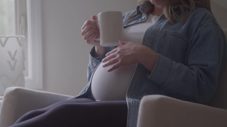 A pregnant woman sits in a chair rubbing her baby bump