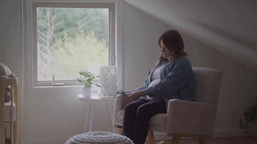 Pregnant woman sitting on an armchair smiling while holding baby clothes