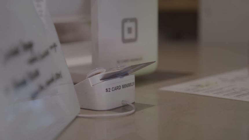 A customer taps a card on a compact reader at the checkout