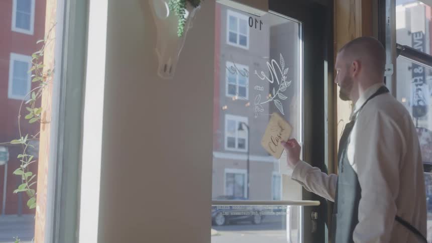 Man turns over the open sign on the glass door of a cafe