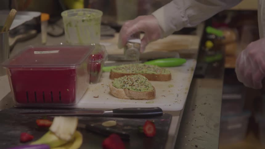 The chef sprinkles pepper on the sandwich