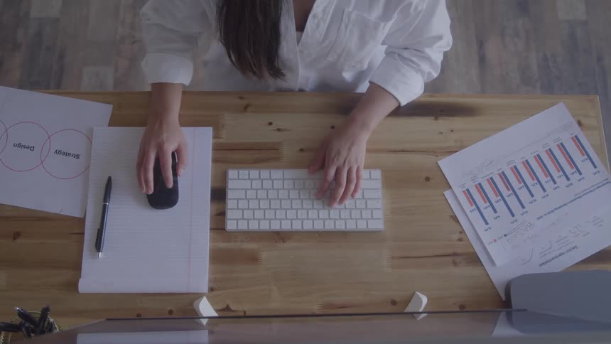 Topdown view of someone typing at a wooden desk papers and graphs spread around