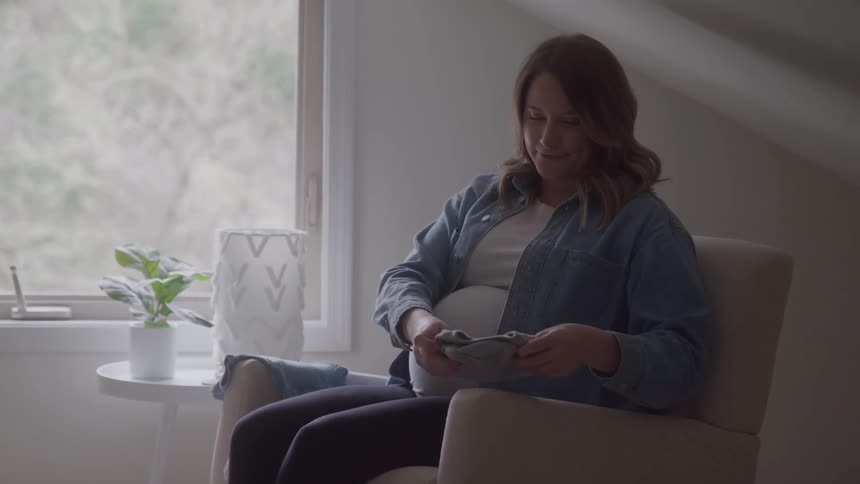 Pregnant woman smiling while holding a gray baby onesie