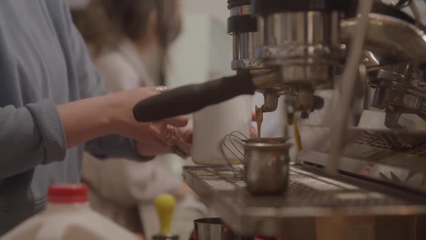 Two baristas work behind a counter as espresso is brewing