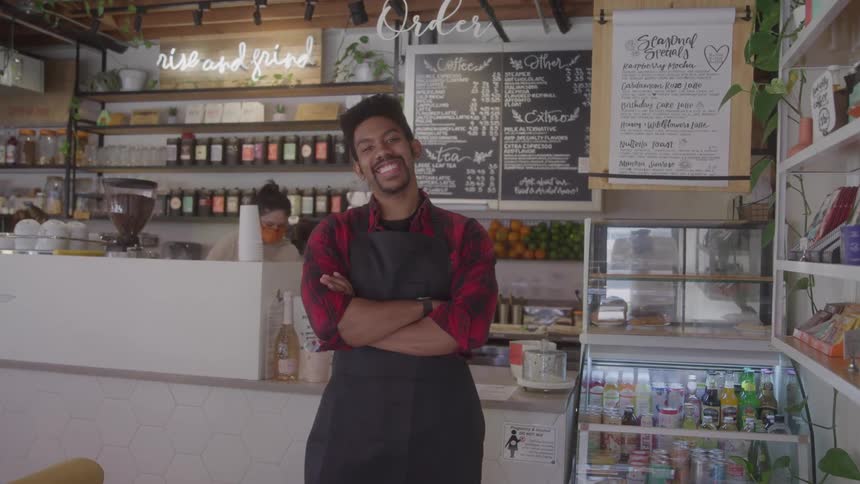 A smiling caf owner stands behind the counter with arms crossed in a bright shop