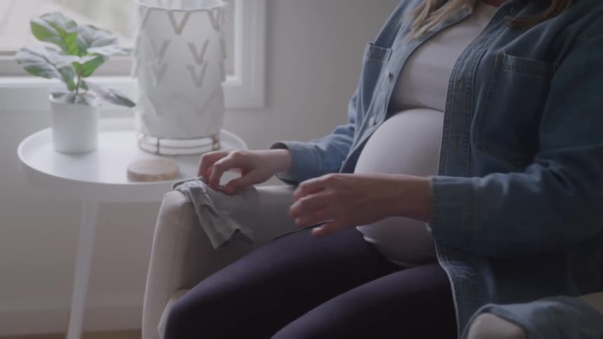 Pregnant woman smiles while holding a gray baby onesie