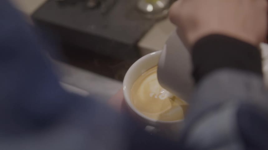 Hand pours steamed milk into a cup of espresso