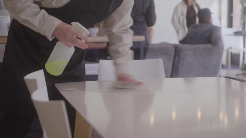 Waiter cleaning the table with spray disinfectant on table in cafe