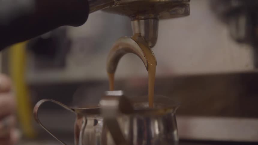 Rich espresso flows smoothly from a machine spout into a metal pitcher