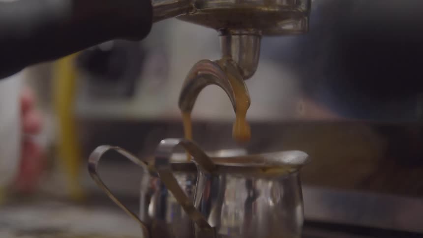 Espresso pours into two metal pitchers in a cafe indoors