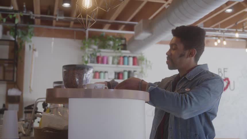 A male customer smiles as he picks up his drink from the counter at a coffee shop