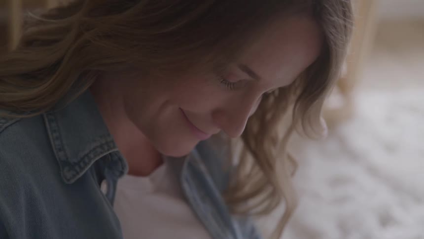A person with long hair and a denim jacket is shown looking down in an indoor setting