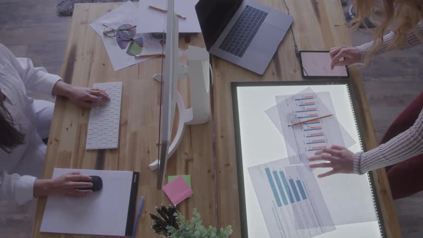 Two people work at an office desk with charts and a computer