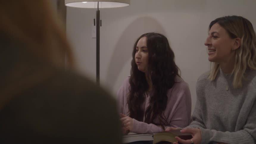 Two women sit talking and holding books indoors