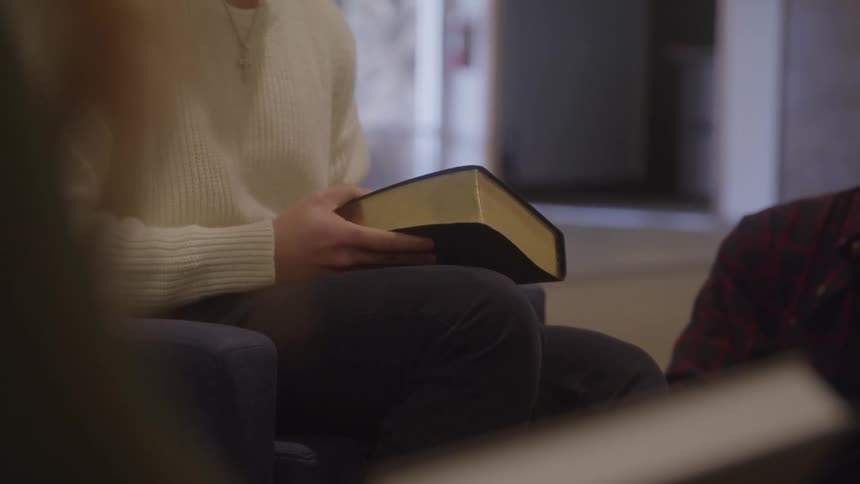 Seated person holds a black book with golden edges