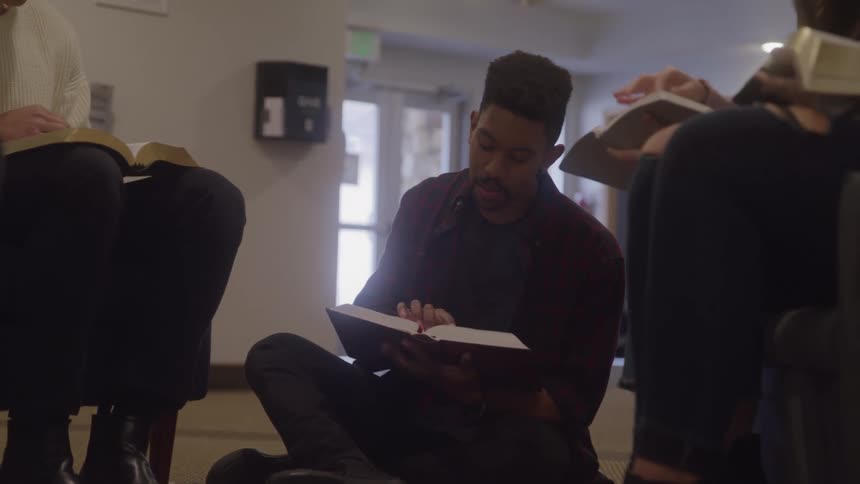 A small group sits together as one person reads aloud from scripture in a quiet gathering