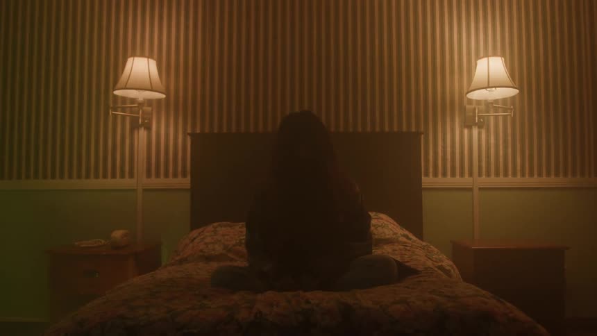 Silhouette of a young woman sitting on the bed in a dim bedroom