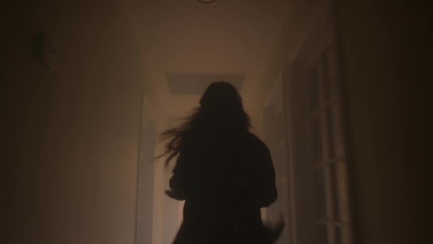 Silhouette of a young woman running through a dark corridor to enter a lit room