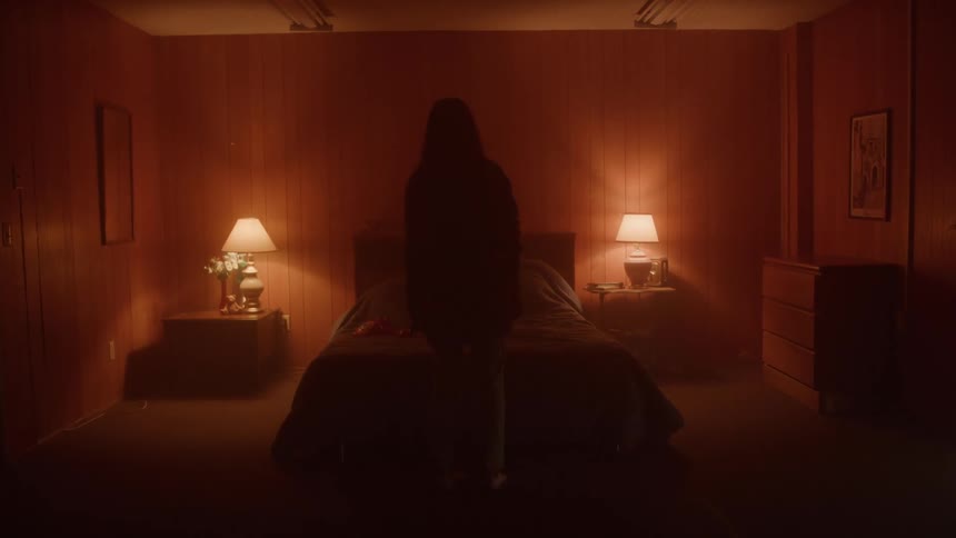 Person stands in front of a bed in a room with soft light and lit lamps