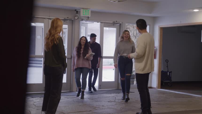 People meet at an entryway smiling and welcoming each other inside