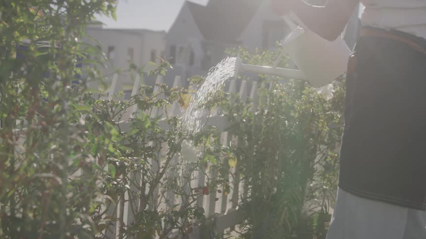 Woman watering plants in the front yard with a white watering can