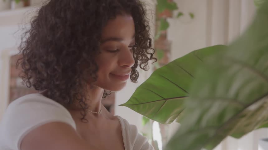 Woman smiles while taking care of a plant indoors