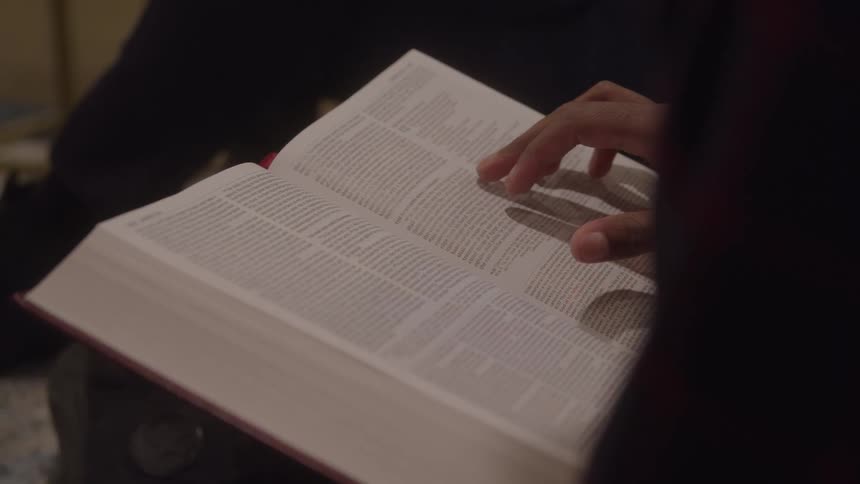 A person runs their finger across the page of the bible while reading