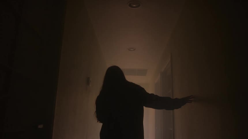 Person walks through a dark hallway with hand on the wall