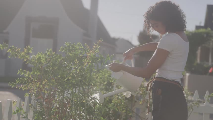 A woman is watering plants in a garden on a sunny day