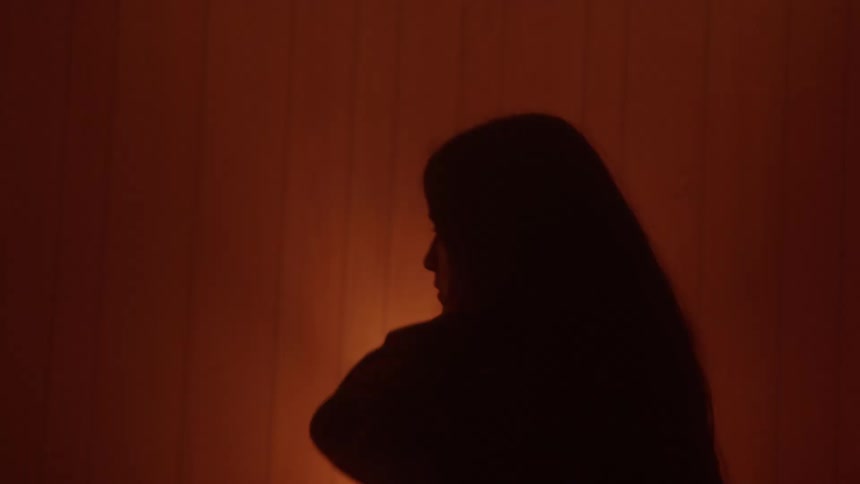 Woman rubs her shoulder while pacing in a wood paneled bedroom at night