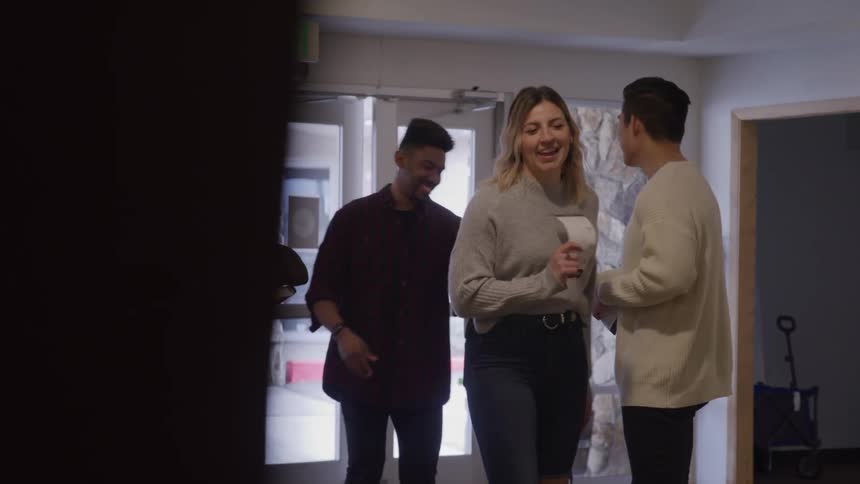Two women and a man walk through the doorway smiling while another man stands inside holding papers and greeting them