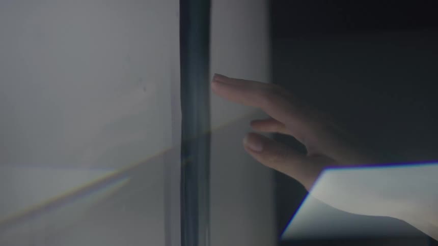 A hand reaches toward a luminous surface catching reflections and subtle geometric light