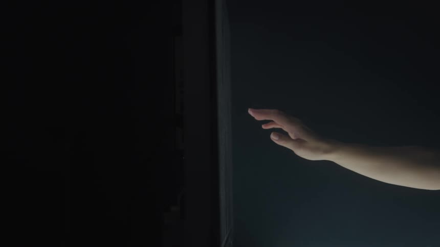 The video shows a persons hand reaching out and touching a dark vertical surface the persons hand and arm are visible on the right side of the frame moving towards the center