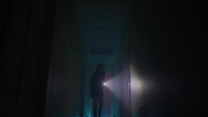 A young woman walking through a dark corridor at night while searching around with a torchlight