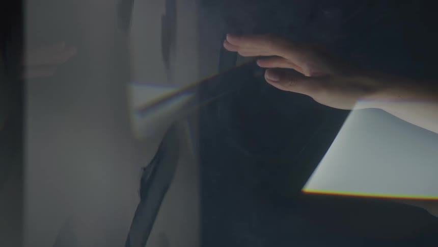 A hand is shown in a close view reaching toward a screen showing film doodles enveloped in light smoke