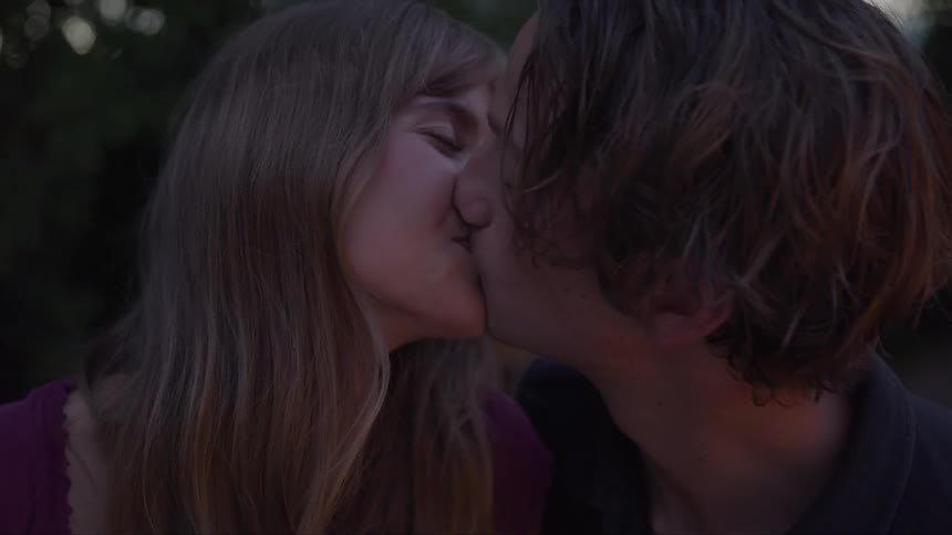 A young man and a young woman are facing each other with their eyes closed smiling as they lean in to kiss each other then pull away and look at each other with happy expressions on their faces