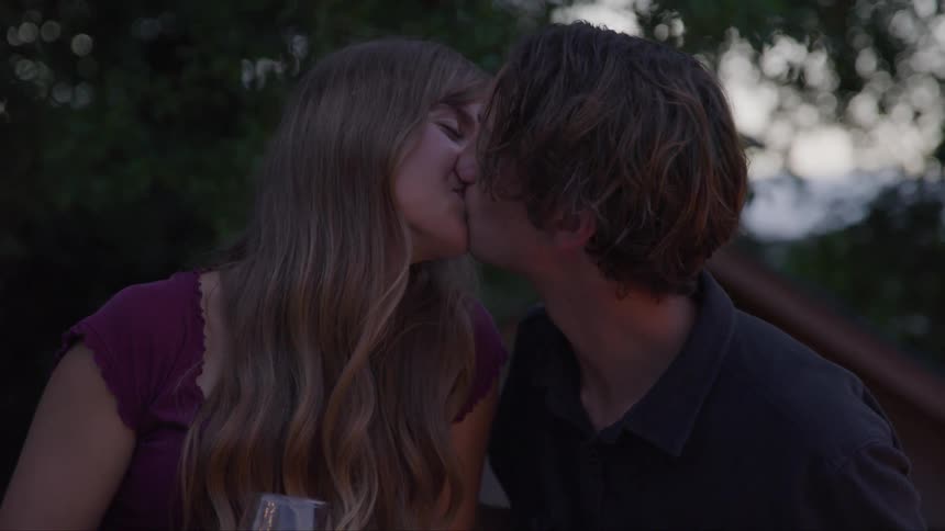 A couple shares a quick kiss outdoors at twilight