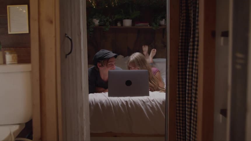 A couple lying on a bed watching a laptop together in a bedroom