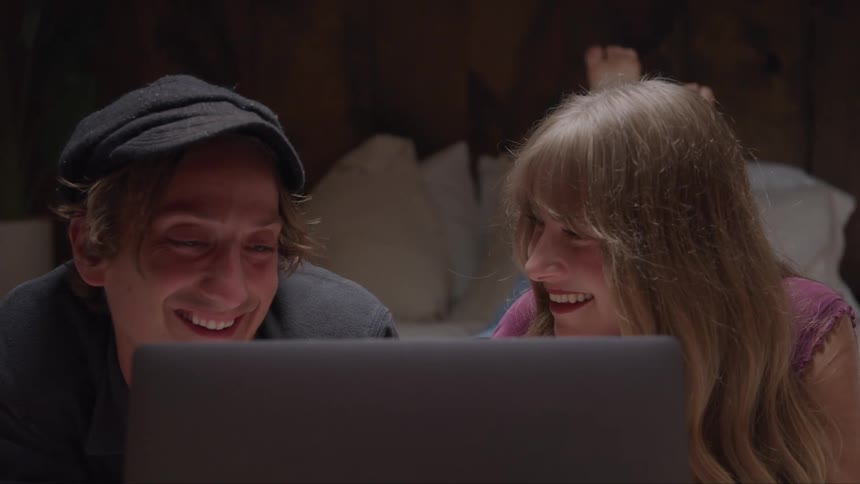 A couple smiles while watching a laptopin the bedroom