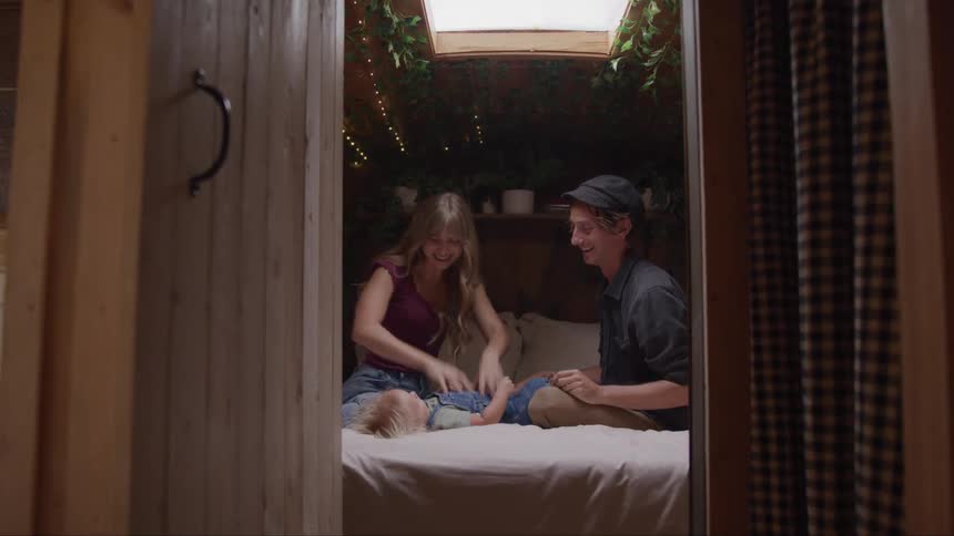A couple tickles their baby laughing on a cozy bed in a wooden cabin